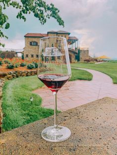 a glass of red wine sitting on top of a stone wall next to a lush green field