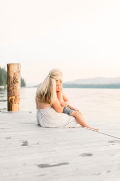 a woman sitting on top of a wooden pier next to the ocean with her hand under her chin