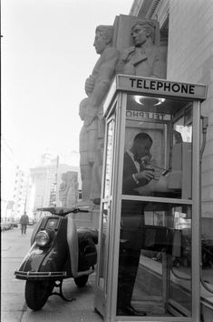 a telephone booth on the side of a street with a man in it looking at his cell phone