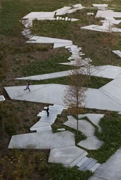 an aerial view of some concrete steps in the grass with trees and people walking on them