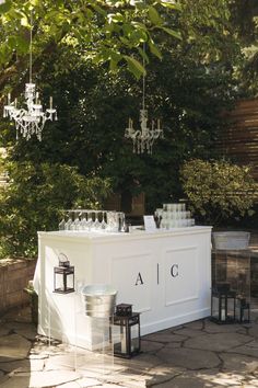 an outdoor bar set up with wine glasses on it and chandeliers hanging from the trees