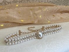 Our most luxurious adornment to date; this faux-pearl-beaded choker necklace has double rows of pearl beads adorned with glass crystal accents, a large encircled faux pearl cabochon, and gold colored adjustable hardware to fit your neck perfectly. Sizing: One Size Neck Circumference 12-16 Inches / 30-40 CentimetersAdjustable Claw Clasp Closure Elegant Gold Choker With Faceted Beads, Gold Beaded Chain Pearl Choker, Gold Beaded Pearl Charm Choker Necklace, Vintage Pearl Choker With Pearl Chain, Vintage Pearl Beaded Choker, Elegant Beaded Pearl Charm Choker, Vintage Adjustable Pearl Choker, Fantasy Shop, Beaded Choker Necklace