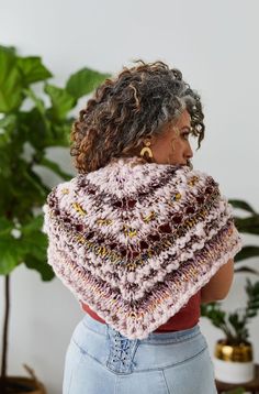 a woman with curly hair is wearing a crocheted shawl and has her back turned to the camera