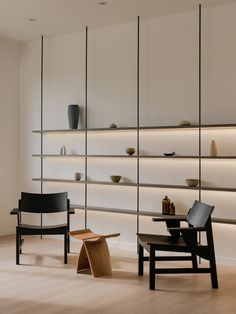 two chairs in front of shelves with vases and bowls on them, one is black and the other is white