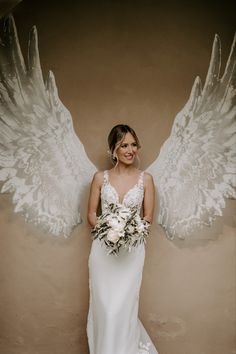 a woman in a wedding dress with angel wings on her head and bouquet in her hand