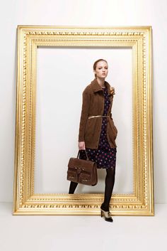 a woman standing in front of a gold frame holding a brown bag and wearing black tights