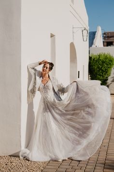 a woman in a long white dress is standing by a wall and posing for the camera