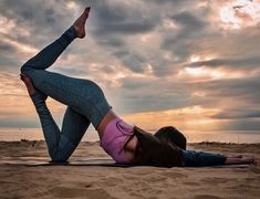 a woman doing yoga on the beach with her feet up in the air as she stretches