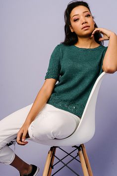 a woman sitting on top of a white chair next to a purple wall with her hand under her chin