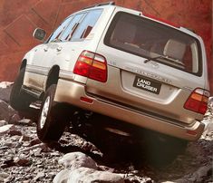 a silver suv parked on top of rocks near a red building with a sign that says land cruiser