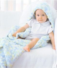 a baby wrapped in a blanket sitting on top of a bed