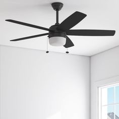 a black ceiling fan in a white room with a window and light on the wall