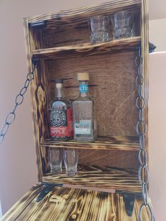 an old wooden shelf with liquor bottles and glasses on the top, hanging from chains