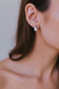 a woman wearing a pair of earrings with pearls on the end of her ear, looking off to the side