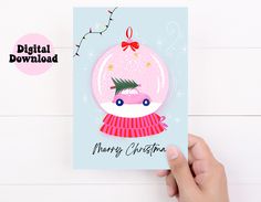 a hand holding up a christmas card with a pink snow globe on it and a red bow