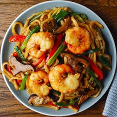 a white plate topped with pasta and shrimp next to a napkin on top of a wooden table