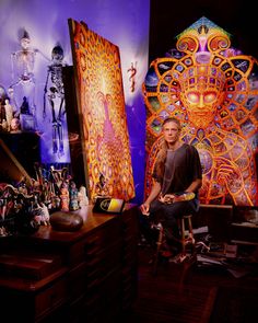 a man is sitting on a chair in front of some art and other items that are on display