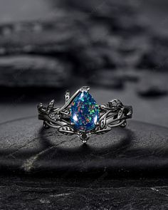 a blue opal ring sitting on top of a black rock with other rocks in the background