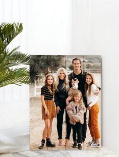 the family is posing for a photo in front of a potted plant and white wall