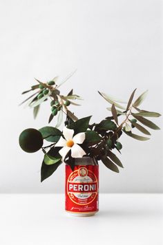 a can filled with flowers and leaves on top of a white table next to a plant