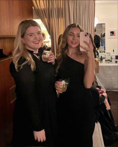 two women standing next to each other holding wine glasses and taking a photo with their cell phone