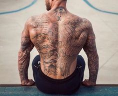 a man sitting on the ground with his back turned to the camera and tattoos all over his body