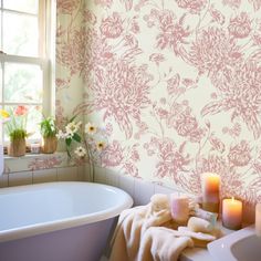 a bath tub sitting under a window next to a white sink and a candle in front of it