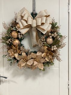 a christmas wreath hanging on the front door with gold ornaments and greenery around it