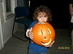 a young boy holding up a carved pumpkin