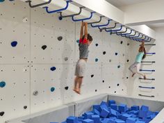 two children are climbing on a rock wall with blue blocks in the foreground and one child is jumping up into the air