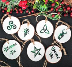 six wooden ornaments with green and white designs on them next to evergreen branches, berries and pine cones