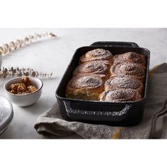 a baking pan filled with cinnamon rolls next to a bowl of walnuts