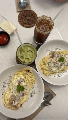 two white plates topped with pasta and sauces next to glasses of liquid on a table