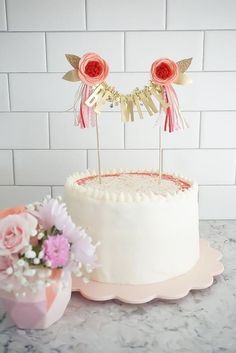 a white cake sitting on top of a table next to a pink flower pot and vase