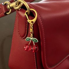 a red leather purse with a gold chain and cherries on the front pocket, along with a keychain