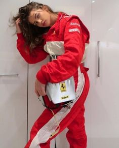 a woman in a red race suit is holding a white bucket and posing for the camera