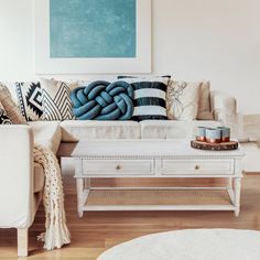 a living room filled with furniture and pillows on top of a wooden floor next to a white coffee table