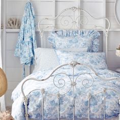 a white bed with blue and white comforter next to a basket filled with flowers