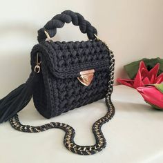 a crocheted black purse sitting on top of a table next to a flower