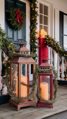 two lanterns on the porch with christmas wreaths around them and lit candles in front