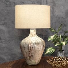 a table lamp sitting next to a vase with a plant in it on top of a wooden table