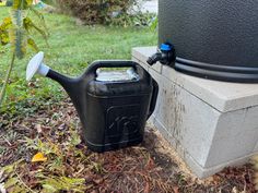 a black watering can sitting on the ground next to a cement block with a hose attached