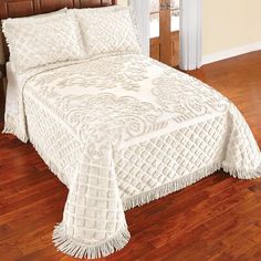 a bed with a white bedspread sitting on top of a hard wood floor