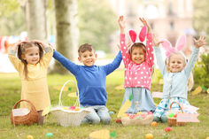 three children sitting on the grass with their hands up in the air and holding easter baskets