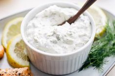 a small bowl of white sauce on a plate with lemons and other food items