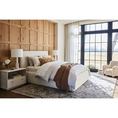 a bedroom with a large window and wooden paneling on the wall, along with a bed