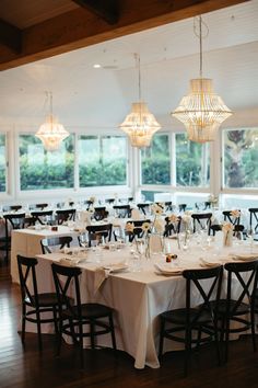 a dining room with tables, chairs and chandeliers hanging from the ceiling in front of large windows