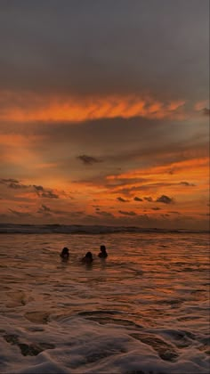 two people swimming in the ocean at sunset