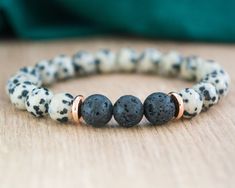 "Our Lava Stone and Dalmatian Jasper Bracelet is a beautiful accessory that offers more than just style. Made with 8 mm lava stones in the center, and Dalmatian Jasper beads, complemented by gold-colored stainless steel spacer discs, this bracelet is designed to help you stay grounded and balanced throughout your day. The beads are strung on a durable stretch cord, allowing for easy on/off fit. The finishing knot is not visible on this item. Whether you're looking for a unique piece of jewelry to add to your collection or a meaningful gift for someone special, this bracelet is sure to impress. Designed to be a perfect gift for her whether you're by her side or miles apart. Your jewelry will arrive in organza bag and gift box. If you want the jewelry with a gift card (see last photo) indica Bohemian Lava Stone Bracelets For Gift, Bohemian Lava Stone Bracelet As Gift, Bohemian Lava Stone Beaded Bracelets Gift, Bohemian Lava Stone Beaded Bracelet Gift, Spiritual Lava Stone Stretch Bracelet Gift, Lava Stone Bracelets With Natural Stones For Gift, Gift Bracelets With Natural Lava Stones, Bohemian Lava Stone Jewelry Gift, Adjustable Lava Stone Stretch Bracelet Gift