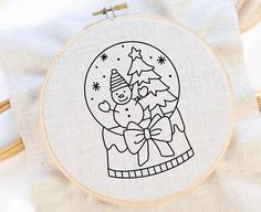 a embroidery pattern with a snow globe and a christmas tree in the center, on top of a white cloth